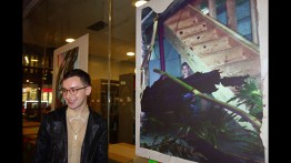 Jackson Stack stands beside one of his photographs at his senior exhibition, "Rooms"