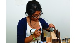 Sarah Benitez, a high school student enrolled in Summer STEM 2014, solders wires to control a motor that performs a step in a Rube Goldberg machine.