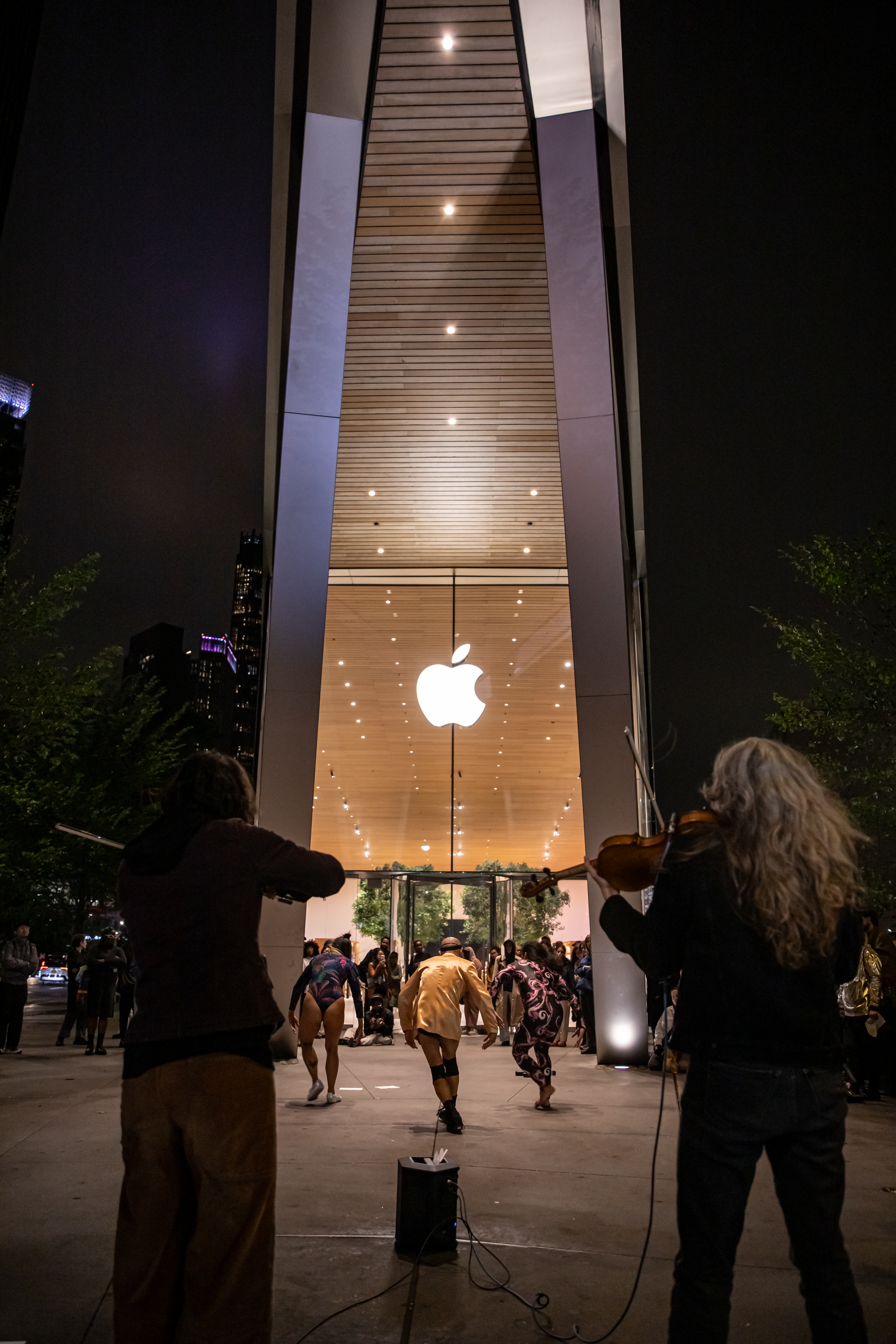 People dancing in front of Apple storefront, two people in foreground playing instruments