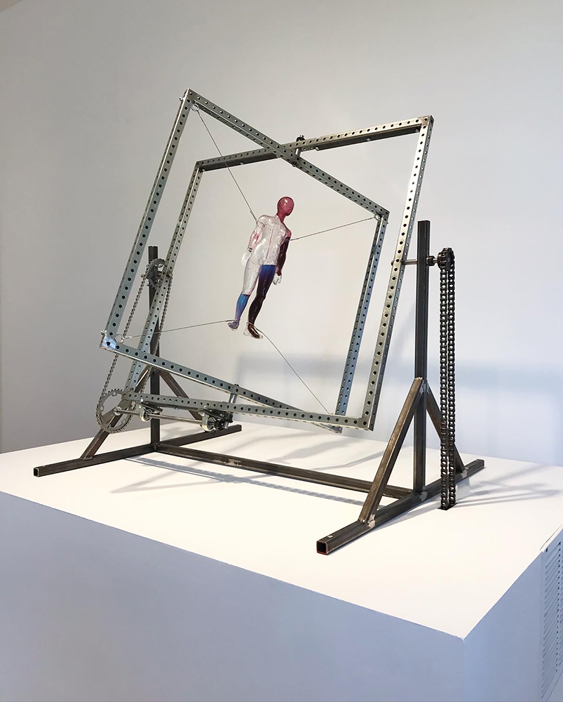 Sculpture sitting on pedestal made of metal components and suspended object in center 