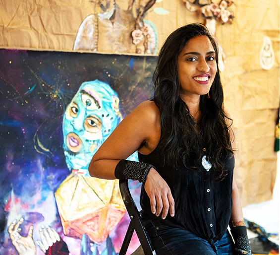 Portrait of Chitra Ganesh seated in front of one of her works