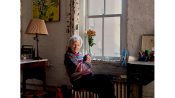 Lois Dodd in her East Village apartment with her painting “Eli In Apple Tree” (1965) above the table.Credit...Vincent Tullo for The New York Times