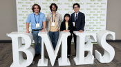 Four students stand behind sculptural letter BMES