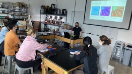 image of a makerspace operator running a workshop on lasercutting modalities in the lab, with a projection behind them and other students in front of them listening