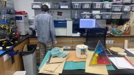 image of a student in makerspace lab operating a lasercutter with some prototypes on a table in front of them