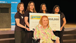 Four students hold a big check behind a woman in a wheelchair