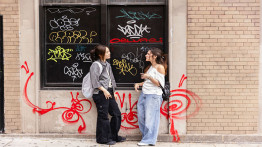 students hanging out in the east village in front of a graffitied wall