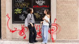 students hanging out in the east village in front of a graffitied wall
