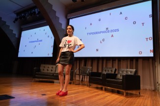 Person on stage with Typographics title card on screen behind them