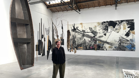 Artist standing by paintings and a boat in a gallery