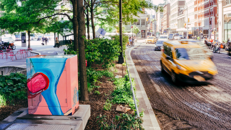 Artwork on box on the left of street as cab passes by public work