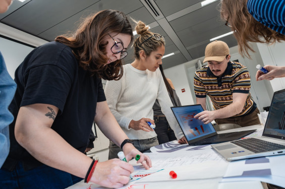 Cooper Union students collaborating over drawings, a tablet, and laptops.