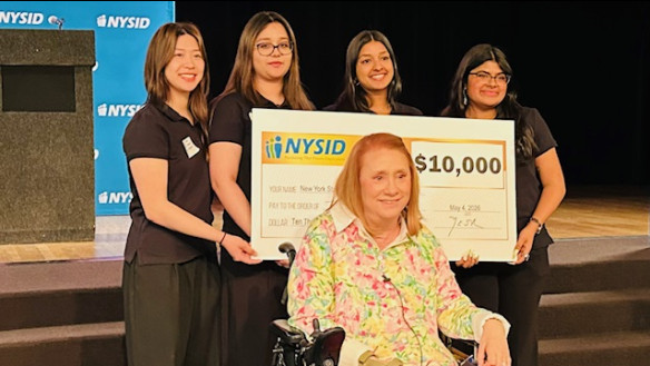 Four students hold a big check behind a woman in a wheelchair